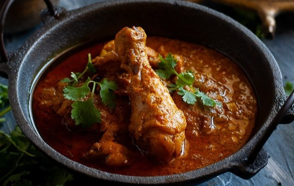 Chicken leg in a black bowl with red curry sauce and few bits of cilantro to garnish
