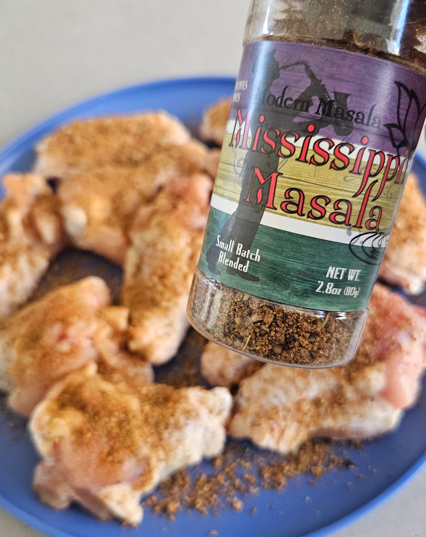 Bottle of seasoning being sprinkled onto chicken pieces on a blue plate.