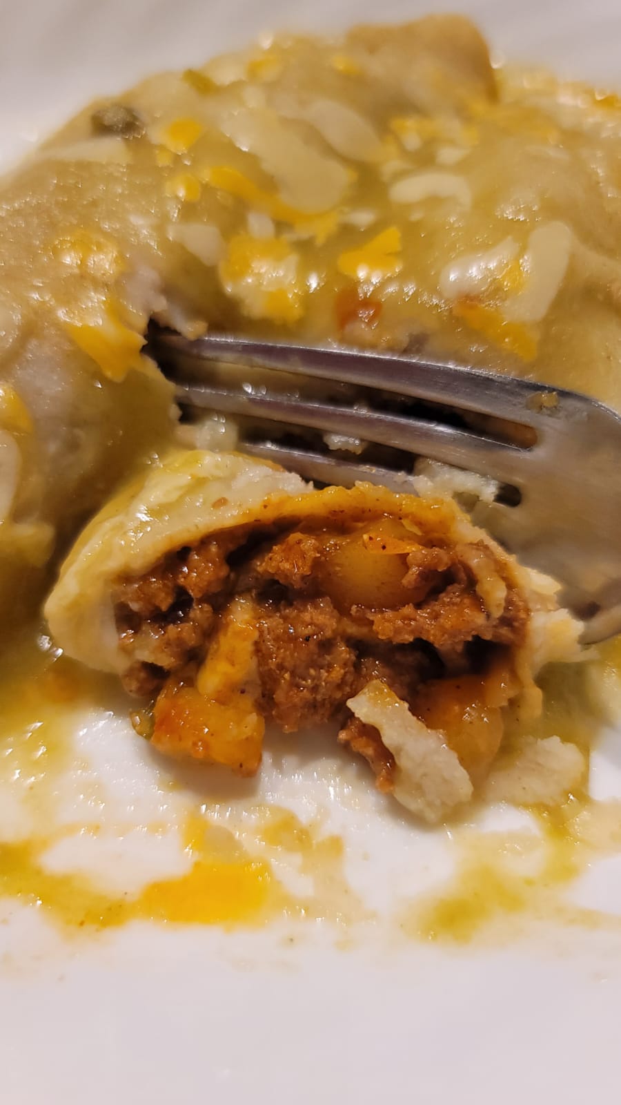 picadillo stuffed enchilada with green sauce and cheese ready to eat with a forkl delicious