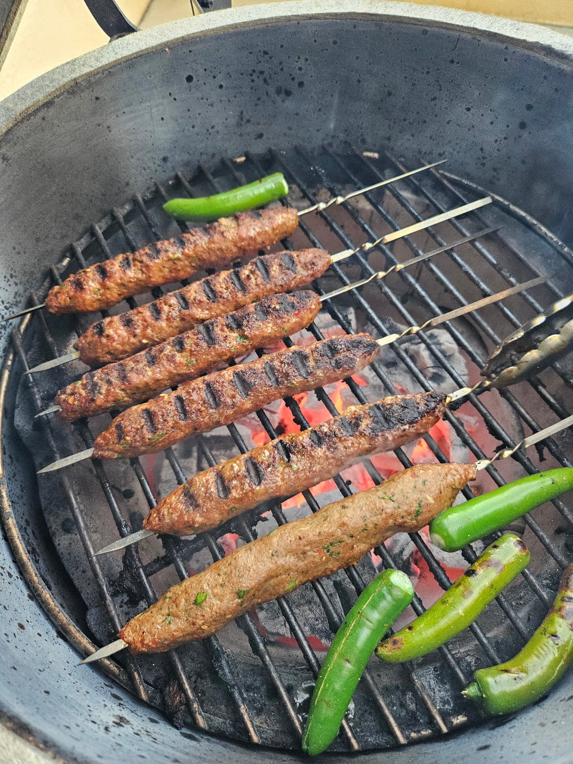 skewered kababs on a grill with green chilis cooking with grill marks 