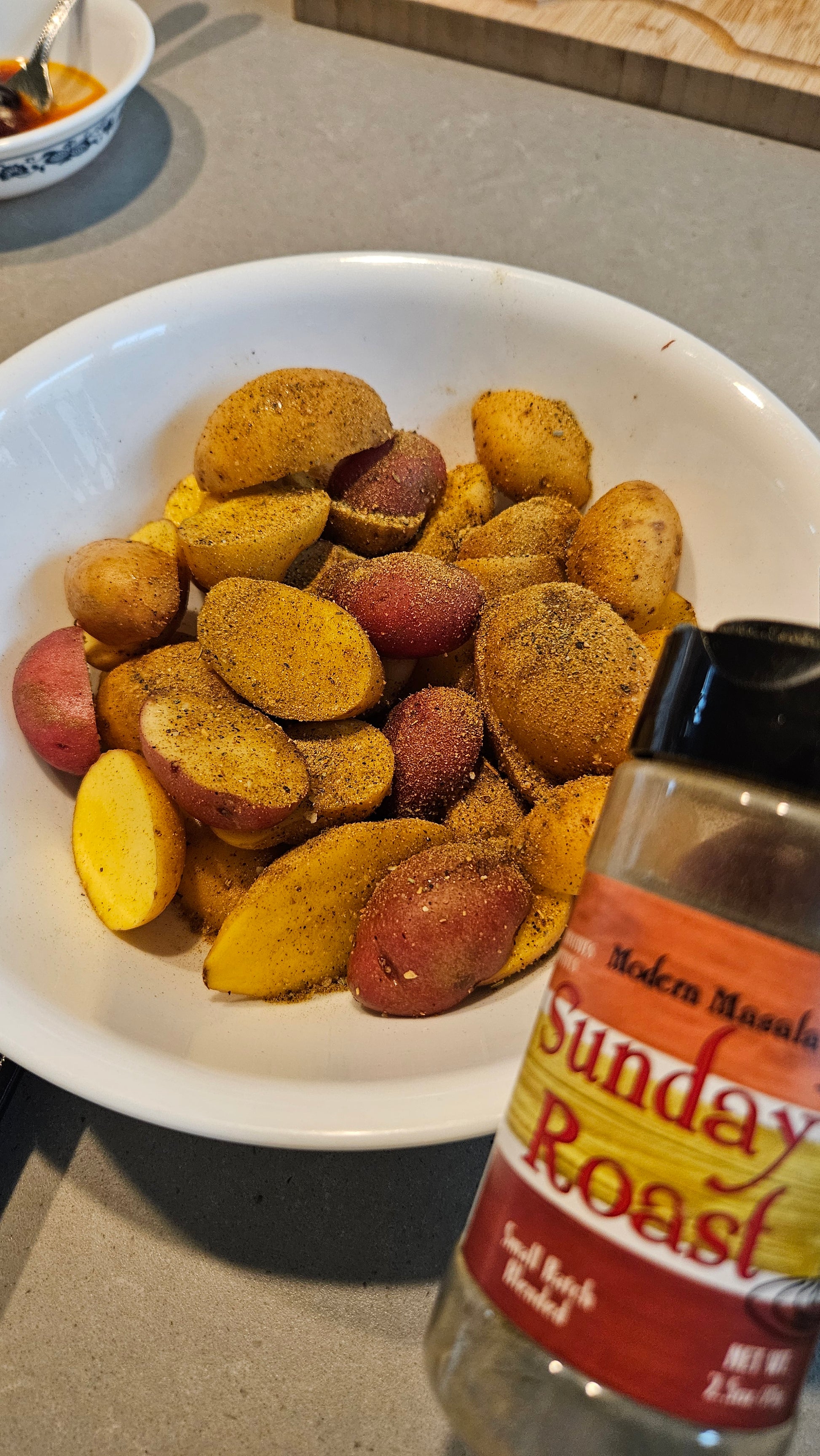 Potatoes  in a bowl with a bottle of Sunday Roast seasoning food in the background.