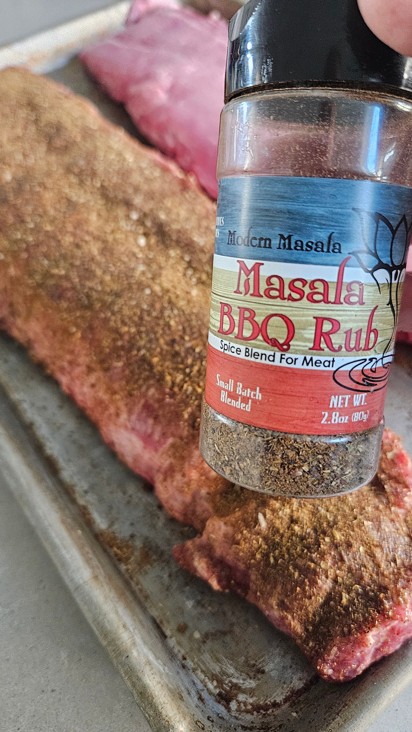 BBQ rub seasoning bottle in front of a rack of baby back ribs with seasoning on it ready for cooking 
