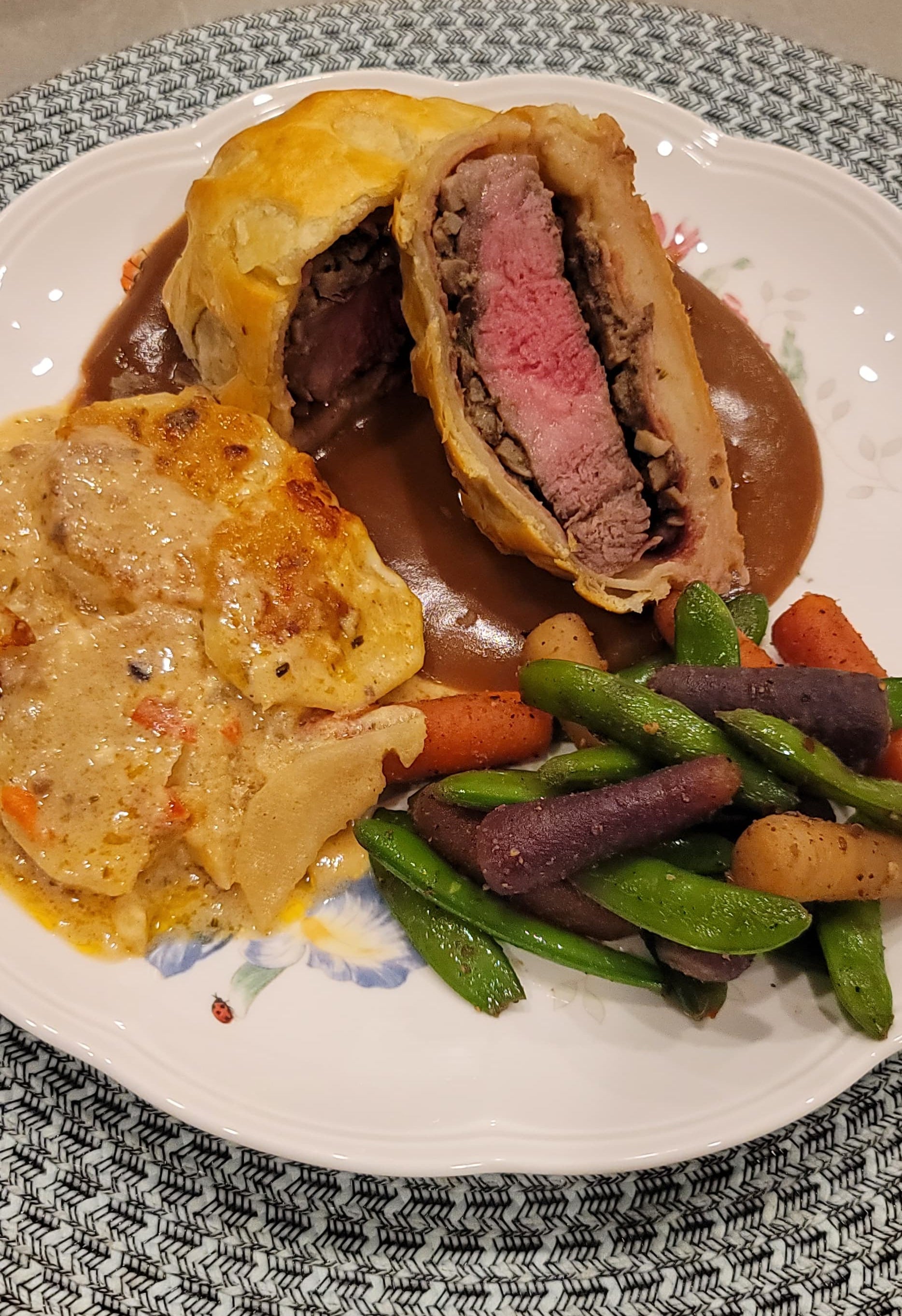 Beef wellington with scallops potatoes and green beans with heirloom carrots  on a white plate