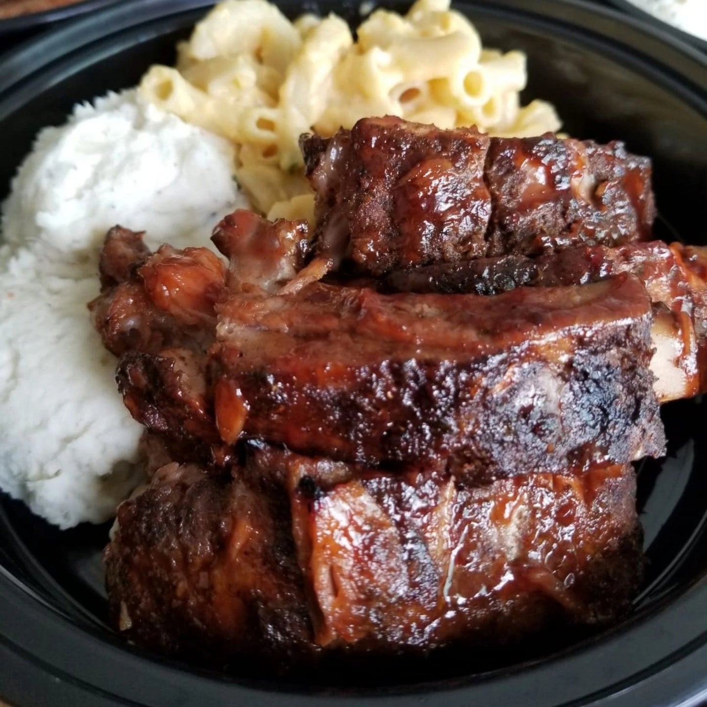 bbq ribs in a bowl with mash potato and mac and cheese in the background image